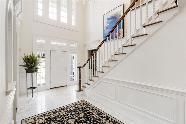 foyer featuring a decorative wall, wainscoting, stairway, and a towering ceiling