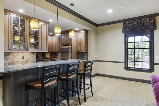 kitchen featuring tasteful backsplash, crown molding, dark stone counters, stainless steel built in fridge, and a kitchen breakfast bar