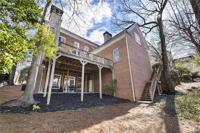 back of property with stairs, a chimney, brick siding, and a wooden deck