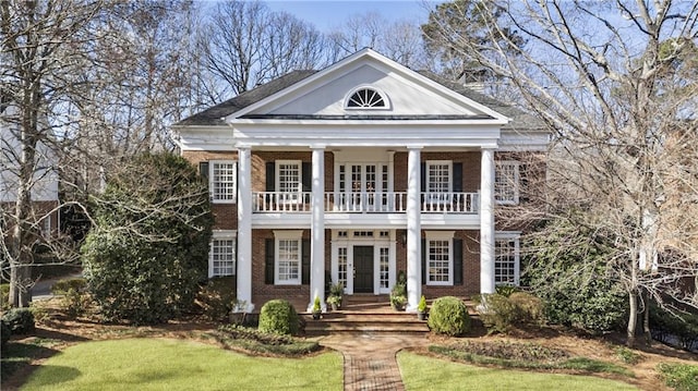 neoclassical home with brick siding, french doors, a front lawn, and a balcony