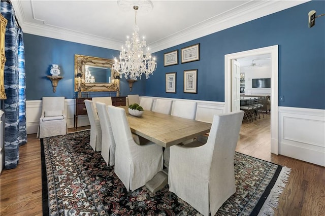 dining space with a wainscoted wall, ornamental molding, an inviting chandelier, and wood finished floors