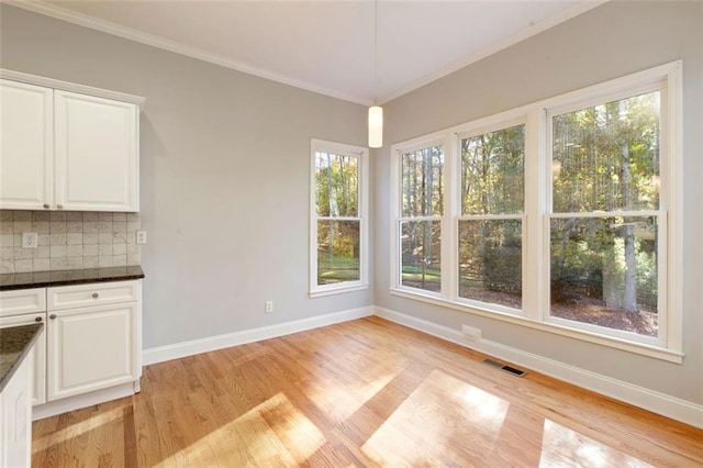 unfurnished dining area featuring crown molding, light wood-style flooring, baseboards, and visible vents