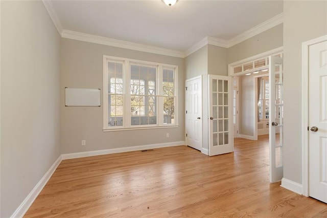 spare room with crown molding, light wood-style floors, baseboards, and french doors