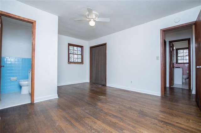 unfurnished room featuring ceiling fan, a wealth of natural light, dark hardwood / wood-style flooring, and tile walls