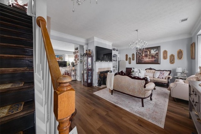 living area featuring crown molding, dark wood finished floors, a fireplace, a notable chandelier, and visible vents