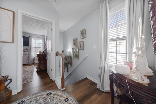 hall featuring dark wood-type flooring, baseboards, and an upstairs landing