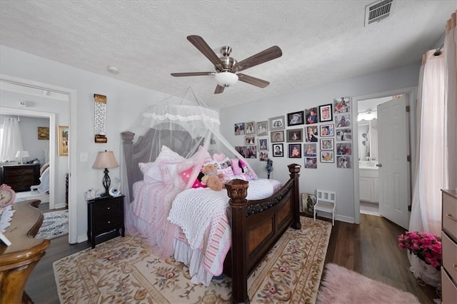 bedroom featuring ceiling fan, a textured ceiling, ensuite bathroom, visible vents, and dark wood-style floors