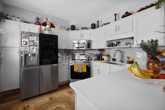 kitchen featuring stainless steel appliances, a sink, white cabinets, light stone countertops, and open shelves