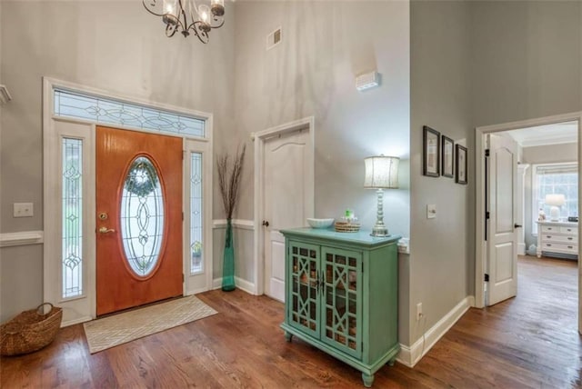 foyer entrance featuring dark wood-type flooring, a chandelier, and a towering ceiling