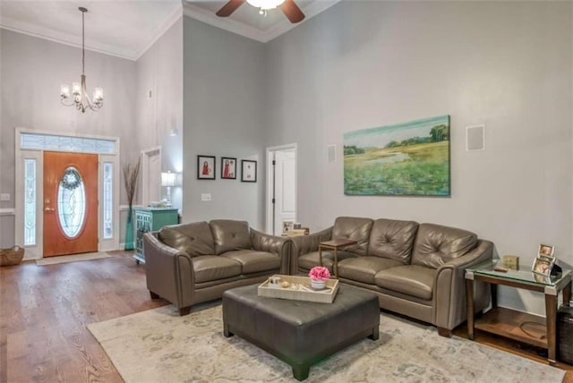 living room with a towering ceiling, crown molding, hardwood / wood-style flooring, and ceiling fan with notable chandelier