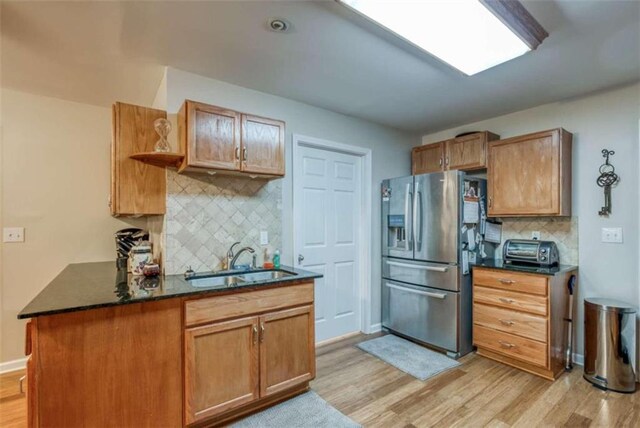 kitchen featuring tasteful backsplash, dark stone countertops, sink, stainless steel fridge with ice dispenser, and light hardwood / wood-style flooring