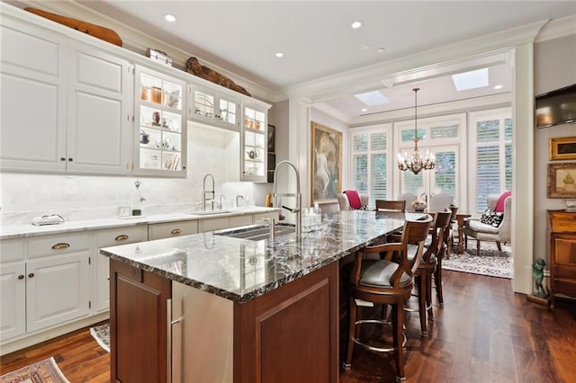 kitchen with crown molding, a center island with sink, white cabinetry, and an inviting chandelier