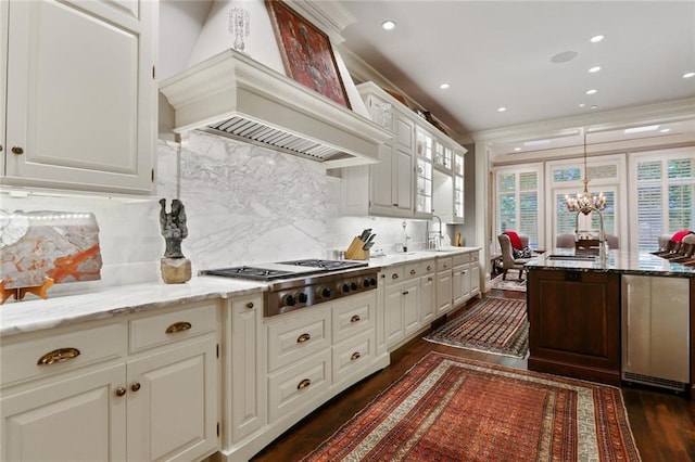 kitchen with light stone countertops, backsplash, a notable chandelier, premium range hood, and white cabinets