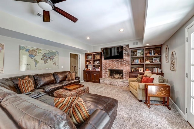 living room with brick wall, light colored carpet, ceiling fan, built in shelves, and a fireplace