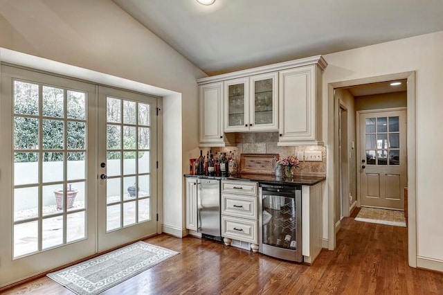 bar featuring french doors, vaulted ceiling, dark wood-type flooring, beverage cooler, and tasteful backsplash