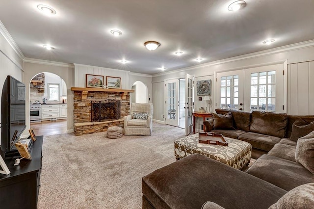 carpeted living room featuring crown molding, french doors, and a stone fireplace