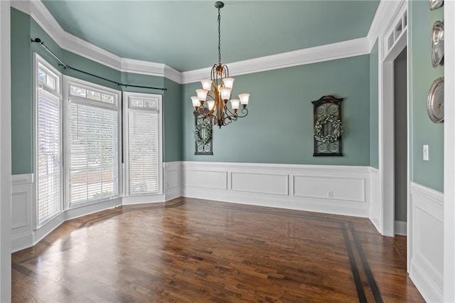 empty room featuring an inviting chandelier, ornamental molding, and dark wood-type flooring