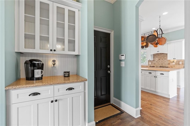 kitchen featuring hardwood / wood-style flooring, light stone countertops, crown molding, white cabinets, and backsplash