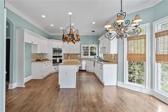 kitchen featuring hanging light fixtures, white cabinetry, backsplash, stainless steel appliances, and a kitchen island