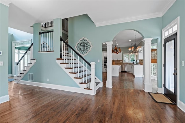 foyer featuring a notable chandelier, crown molding, dark wood-type flooring, and ornate columns