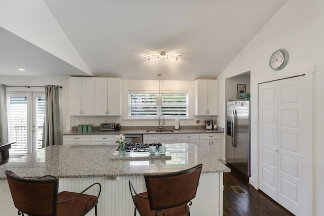 kitchen with lofted ceiling, dark hardwood / wood-style floors, stainless steel appliances, white cabinets, and a breakfast bar area