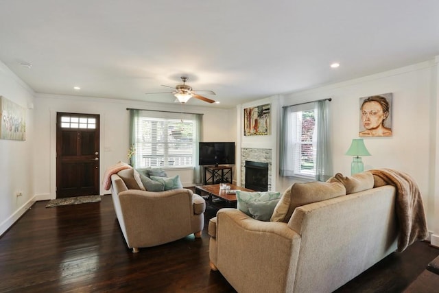 living room with a stone fireplace, ceiling fan, dark hardwood / wood-style flooring, and a healthy amount of sunlight