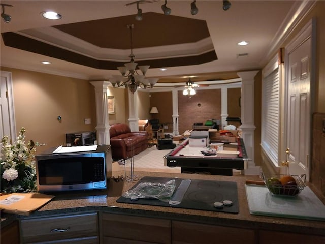 interior space featuring ornate columns, track lighting, a raised ceiling, and ceiling fan with notable chandelier