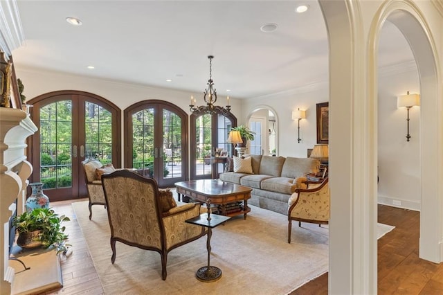 living room featuring crown molding, a notable chandelier, light hardwood / wood-style floors, and french doors