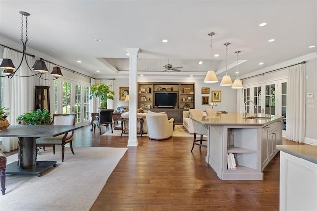 kitchen featuring ceiling fan with notable chandelier, a kitchen island with sink, white cabinets, dark hardwood / wood-style flooring, and pendant lighting