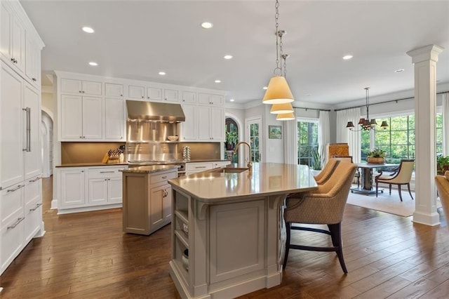 kitchen featuring a kitchen island with sink, dark wood-type flooring, hanging light fixtures, and white cabinets