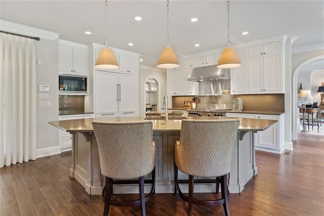 kitchen with hanging light fixtures, built in appliances, a center island with sink, and dark wood-type flooring