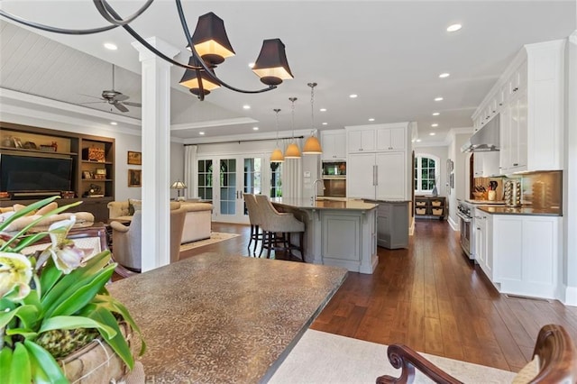 kitchen featuring dark hardwood / wood-style flooring, white cabinetry, a kitchen island with sink, pendant lighting, and ceiling fan with notable chandelier