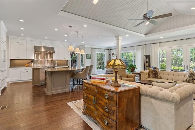 living room with sink, dark wood-type flooring, ornate columns, ceiling fan with notable chandelier, and lofted ceiling