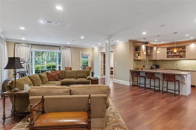 living room featuring dark hardwood / wood-style flooring, crown molding, decorative columns, and sink