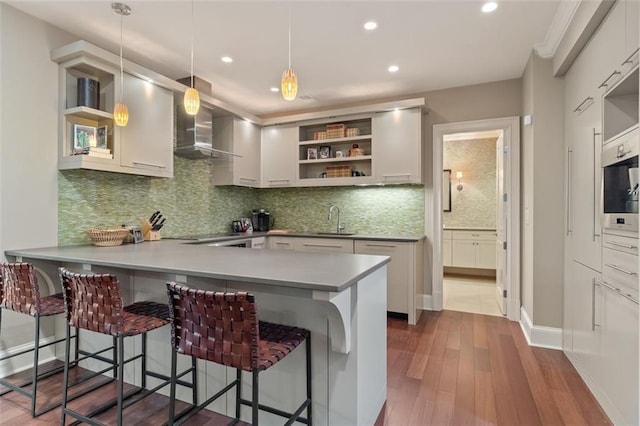 kitchen with white cabinets, a kitchen breakfast bar, wall chimney exhaust hood, and pendant lighting