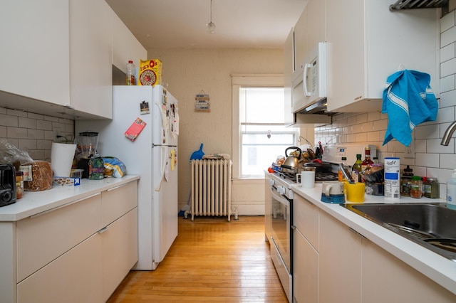kitchen featuring white appliances, radiator, white cabinets, backsplash, and light wood-type flooring