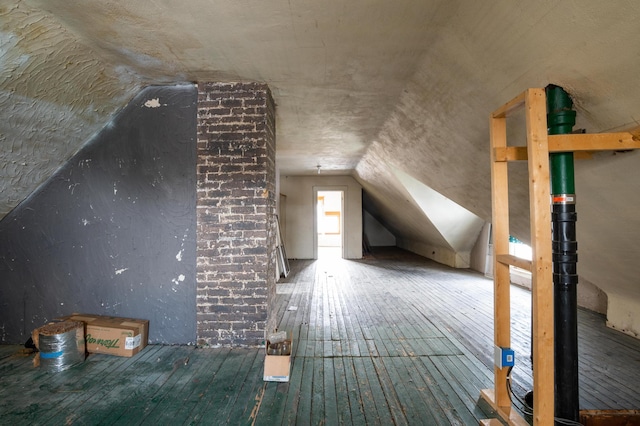 additional living space with dark wood-type flooring, brick wall, and vaulted ceiling