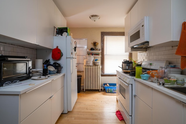 kitchen with radiator, white appliances, light wood-type flooring, and white cabinetry