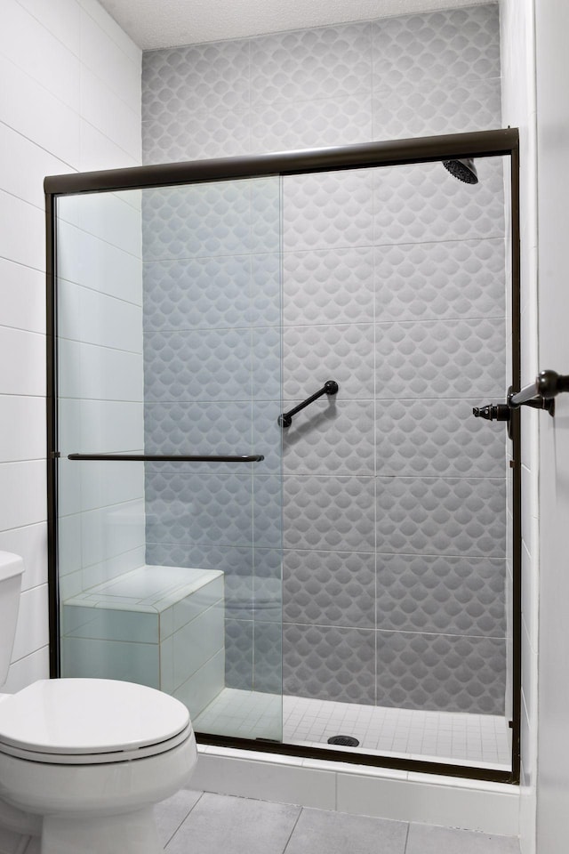 bathroom featuring tile flooring, tile walls, a shower with door, a textured ceiling, and toilet