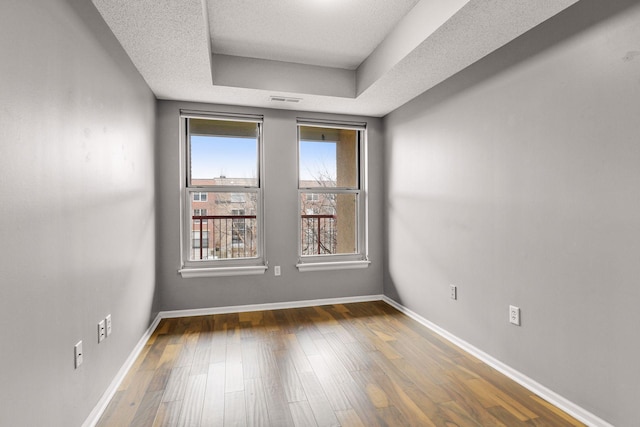 empty room featuring a tray ceiling, a textured ceiling, and dark hardwood / wood-style flooring