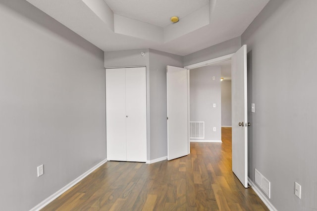 unfurnished bedroom with dark hardwood / wood-style flooring, a closet, and a tray ceiling