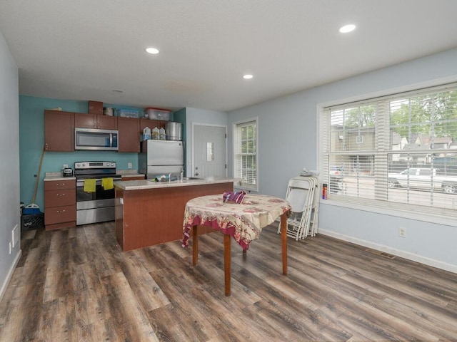 kitchen featuring a kitchen bar, a kitchen island with sink, stainless steel appliances, and dark wood-type flooring