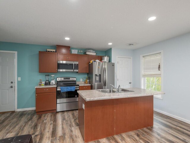 kitchen with dark hardwood / wood-style flooring, appliances with stainless steel finishes, an island with sink, light stone countertops, and sink