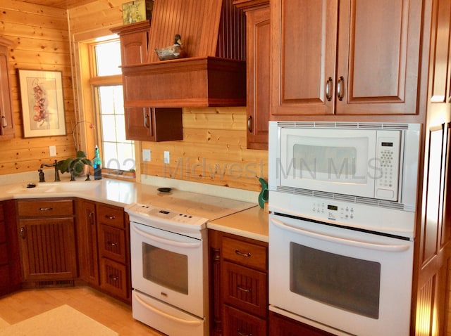 kitchen featuring light hardwood / wood-style floors, wooden walls, sink, and white appliances