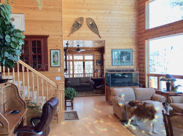 living room with wood walls, light hardwood / wood-style flooring, ceiling fan, and plenty of natural light