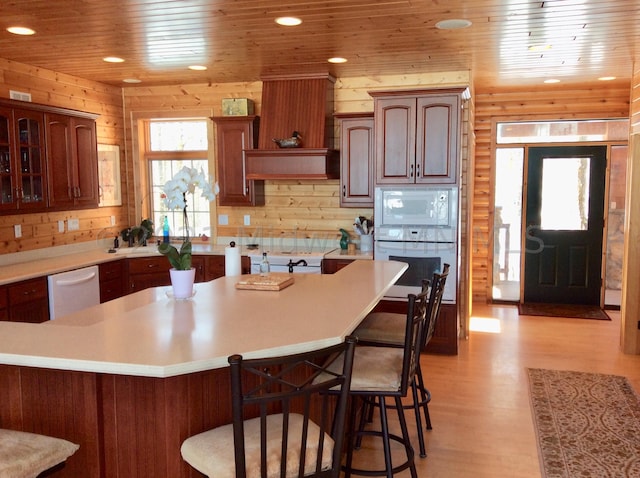 kitchen with wood ceiling, a kitchen bar, light wood-type flooring, white appliances, and wood walls