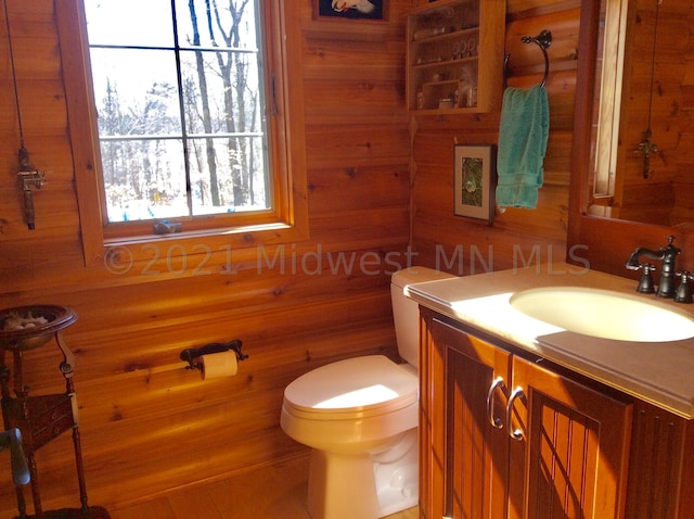 bathroom featuring toilet, vanity, and wooden walls