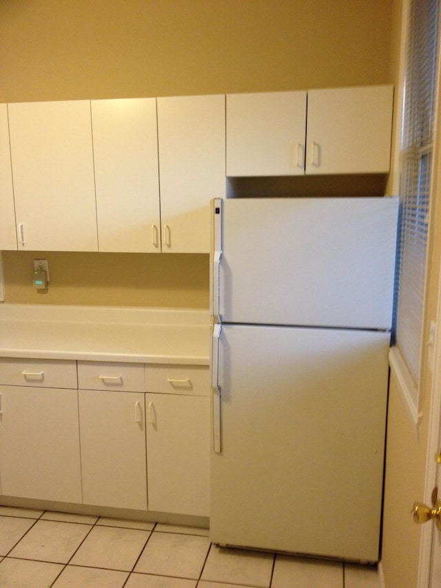 kitchen featuring white refrigerator, light tile flooring, and white cabinetry