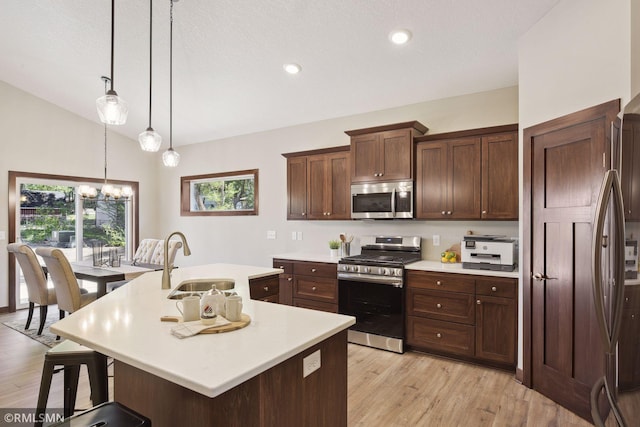 kitchen featuring a center island with sink, stainless steel appliances, light hardwood / wood-style flooring, sink, and vaulted ceiling