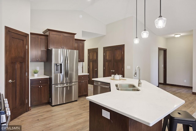 kitchen featuring decorative light fixtures, appliances with stainless steel finishes, a kitchen island with sink, light wood-type flooring, and sink